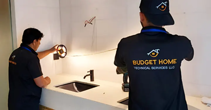 Two members of the Budget Home Fix team in company uniforms working at a kitchen counter.